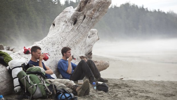 Hikers sit against a giant driftwood log sipping hot tea.