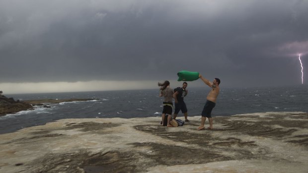 Beachgoers brace against the wind as lightning strikes in the background.