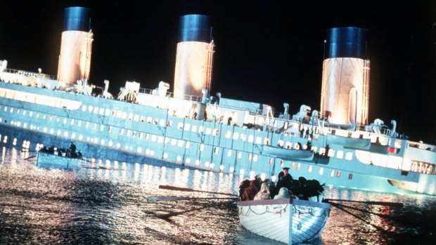 Passengers row to safety aboard a lifeboat as the ill-fated ship sinks in <i>Titanic</i>.