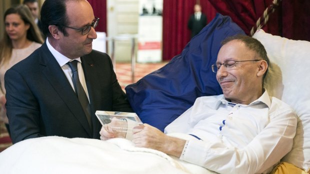 French President Francois Hollande talks with the laureate Claude Emmanuel Triomphe, laying on a bed as he was injured in the November 13 Paris attacks.