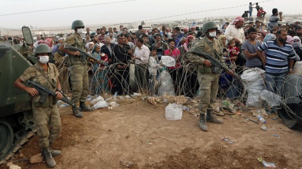 Turkish soldiers stand guard as Syrian Kurdish refugees wait to cross into Turkey.