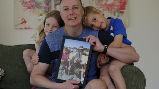 Trevor Hickman at his home in Curtin with his two children Audrey, 8, and Elijah, 6. He is holding a photograph of his wife, Amy, who died of breast cancer last year.