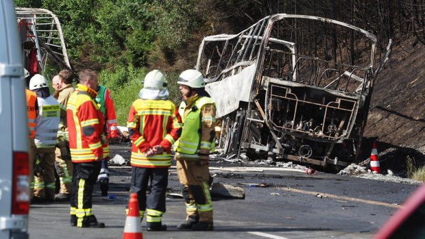 Rescue workers and firefighters stand beside the burnt-out coach.