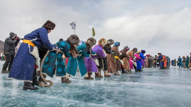 Mongolians dressed in traditional clothing on frozen lake Khovsgol pulling a rope to compete in tug-o-war.