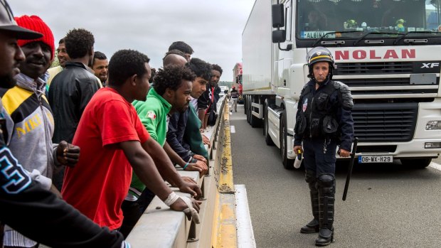 A French riot police officer stands guard as migrants wait to hide in trucks heading for England.