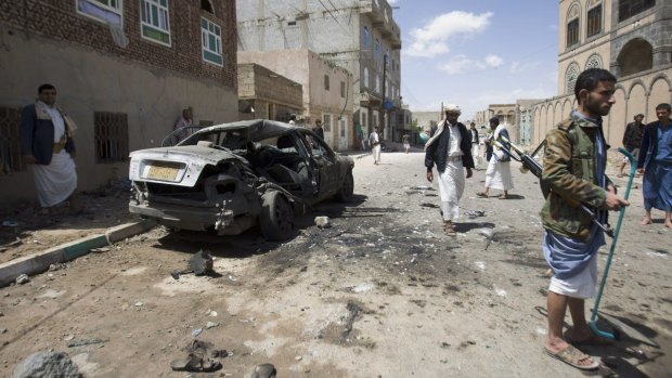 Shiite rebels, known as Houthis, stand near a damaged car after the bombing in Sanaa.
