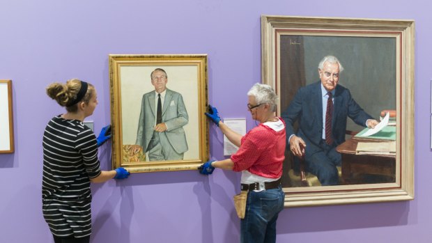 National Portrait Gallery staff hang a portrait of Malcolm Fraser next to a portrait of Gough Whitlam on Friday.