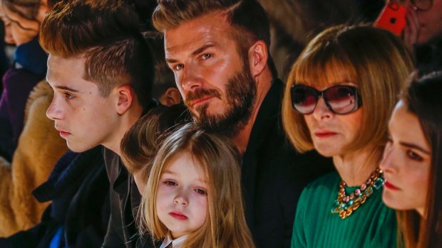 Stealing the show: David Beckham sits next to US Vogue editor Anna Wintour with daughter, Harper on the lap.