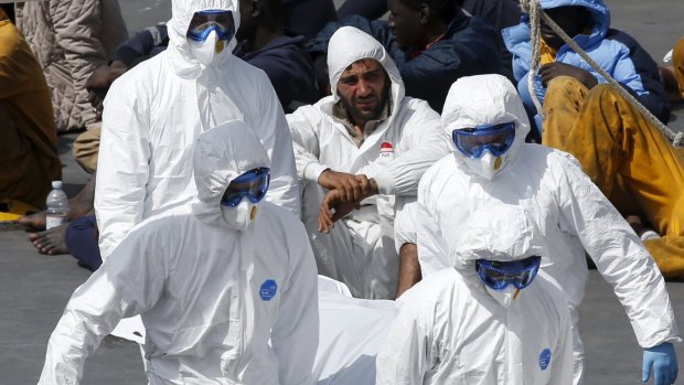 Armed Forces of Malta personnel in protective clothing carry the body of a dead immigrant off the Italian coastguard ship Bruno Gregoretti on Monday.