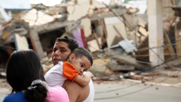 A man holds a child next to a collapsed building in Portoviejo.