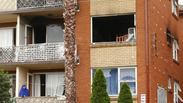 A woman looks out from her balcony under the apartment damaged by fire last night in Lakemba.