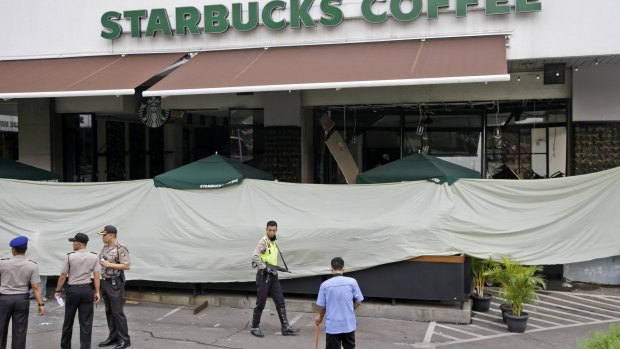 Police and officials gather in the parking lot outside the damaged Starbucks cafe where Thursday's attack occurred in Jakarta.