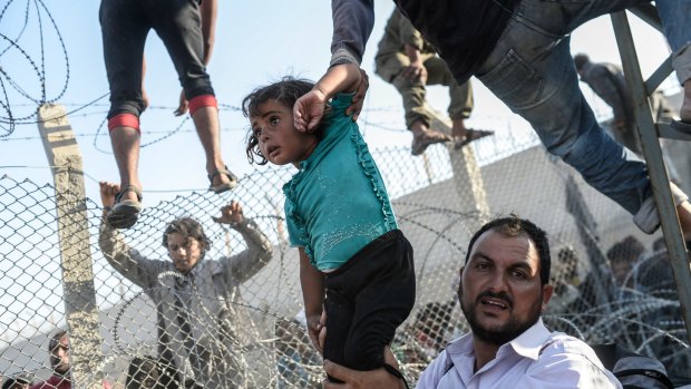 A Syrian child fleeing the war is lifted over border fences to enter Turkish territory illegally, near the Turkish border crossing at Akcakale in Sanliurfa province on June 14, 2015.