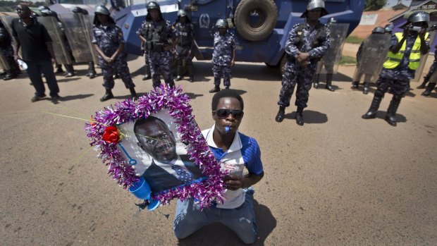 A supporter holds a poster of opposition leader Kizza Besigye in front of a line of riot police near the village of Kyanji, outside Kampala, on Tuesday. 