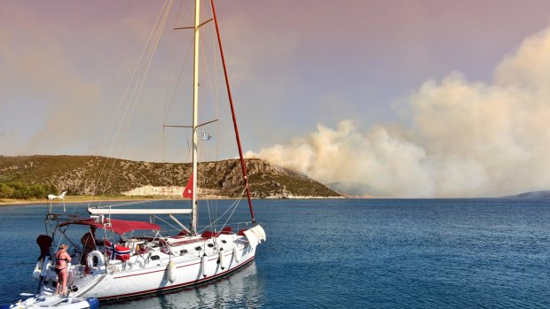 Tourists on a sailing boat as a wildfire burns on the mountain near the town of Nafplio, about 140 kilometres south-west of Athens on Friday.