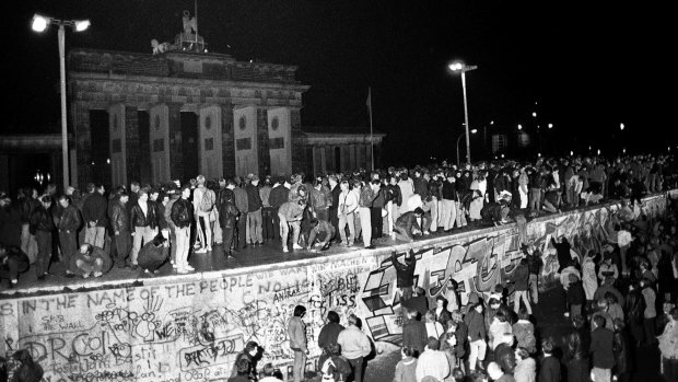 East and West German citizens celebrate as they climb the Berlin wall at the Brandenburg Gate on November 9, 1989.