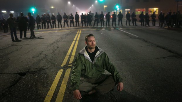 A man who identified himself as Mike V. sits in the street after being blocked by a line of police officers on the second night of demonstrations.