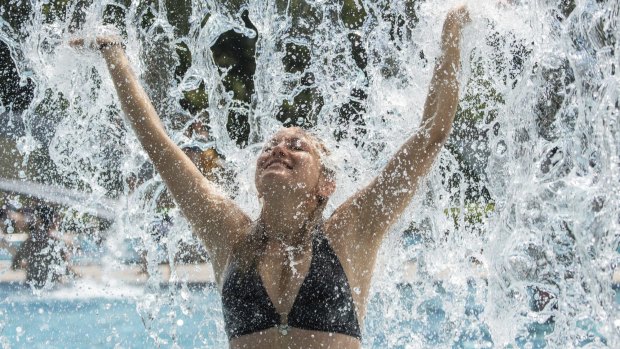 A young woman stands under an artificial waterfall as summer temperatures peak in Germany.