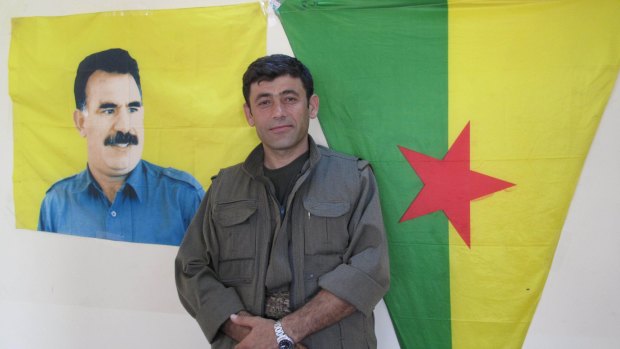 Commander Badr Khan standing under a flag featuring the image of Abdullah Ocalan, the imprisoned PKK leader.
