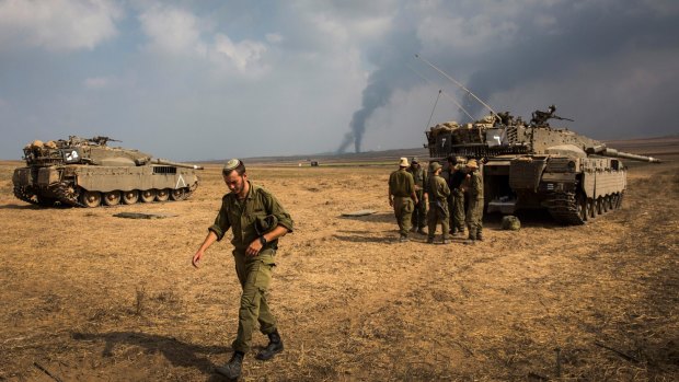 Israeli soldiers stand near their tank while smoke rises from Gaza during Operation Protective Edge in July 2014.