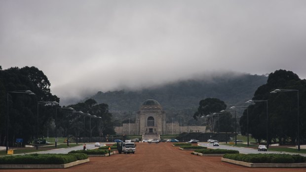Fog rolls in on Anzac Parade as workers tidy the gardens ahead of Anzac Day.
