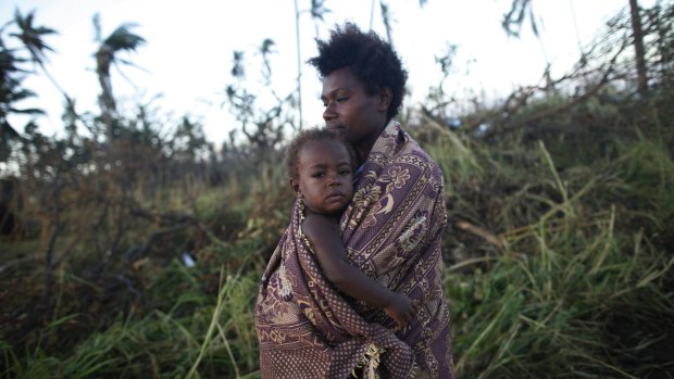 A woman carrying her baby walks past fallen trees in Tanna.