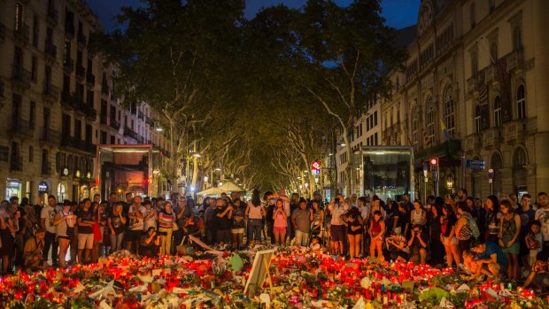 People stand next to candles and flowers placed on the ground, after a terror attack that left many killed and wounded in Barcelona.