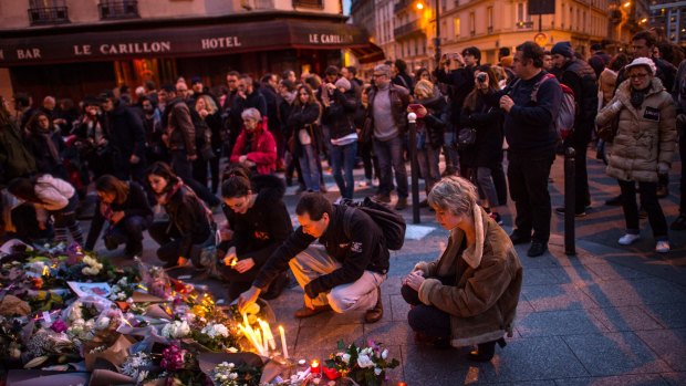 Mourners leave candles in front of the Petit Cambodge restaurant with the Le Carillon restaurant in the background.
