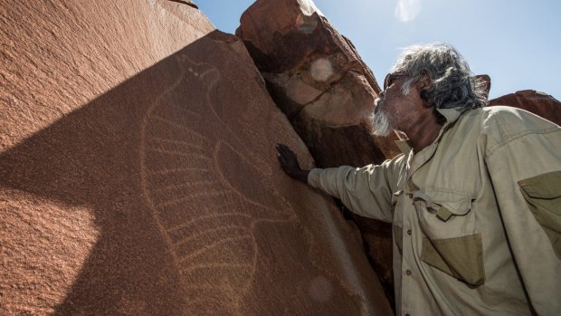 Senior cultural ranger at Murujuga National Park, Jakari Togo, stands next to a rock carving of a thylacine on the Burrup Peninsula, Western Australia.