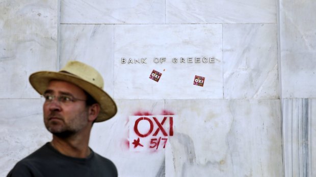 A man walks past the Athens headquarters of Bank of Greece where graffiti and stickers reading "No" can be seen.