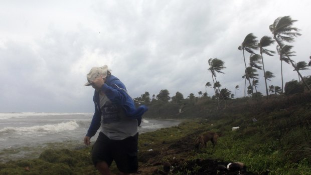 A man walks on the shore against strong winds backdropped by a rough sea as Tropical Storm Erika moves away from the area in Guayama, Puerto Rico.