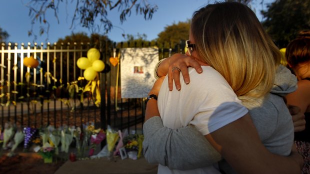 A couple comfort each other at the floral tributes for teacher Stephanie Scott in front of Leeton High School.