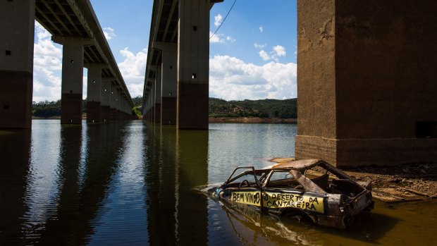 A shell of a car sits in the water with graffiti that reads in Portuguese, "Welcome to the desert of Cantareira", on the banks of the Atibainha reservoir, part of the Cantareira System that provides water to Sao Paulo city.