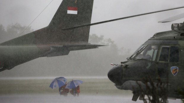 Indonesian Air Force crew members taking part in the search for AirAsia QZ8501 wait out a rain storm under the tail of a cargo plane at the airbase in Pangkalan Bun.
