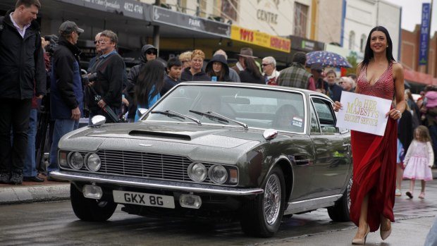 Serena Greaves walks alongside the original Aston Martin DBS from On Her Majesty's Secret Service, driven by owner Sigi Zidziunas during the SpyFest Street Parade on Saturday.