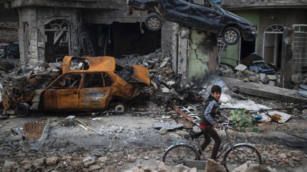 A boy rides his bike past destroyed cars and houses in a neighbourhood recently liberated by Iraqi security forces, on the western side of Mosul, on March 19.