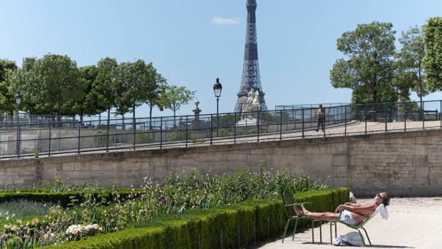 People sunbathe at the Jardin des Tuileries with the Eiffel Tower in the background.