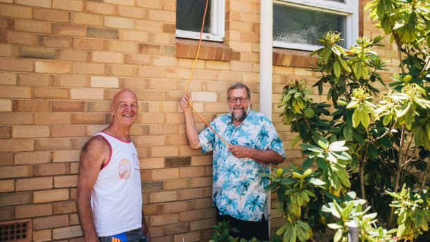 Axel Godeck with his neighbour Jim Croft at home in Campbell. Croft hasn't had power since Friday when a tree damaged the power lines outside his home so Godeck ran a power lead from his home so that Croft could charge his phone.
