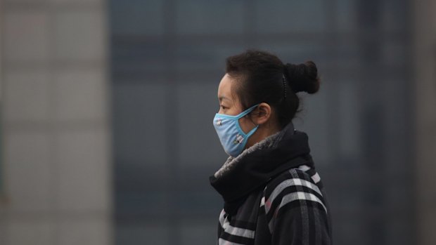 A woman wears a mask as she walks on a street in Beijing.