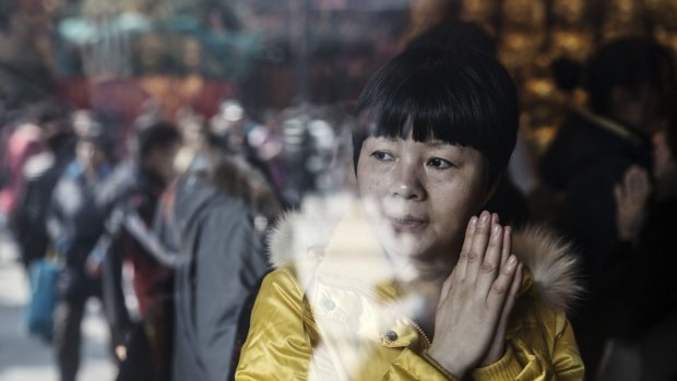 A woman seen through a window prays at Longhua Temple in Shanghai, China, as fears of financial instability rattles the nation.