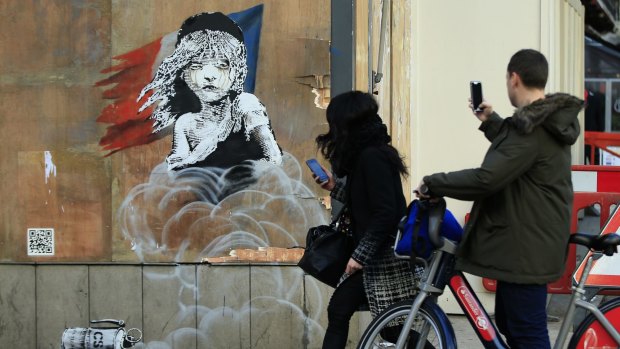 Commuters take photos on their phones of a new artwork by British artist Banksy opposite the French embassy in London on Monday.
