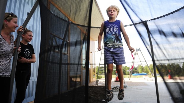 Kayne jumps on the trampoline in the outdoor play area at the Ricky Stuart House in Chifley as his mother Beth and sister Chloe,11, look on. 