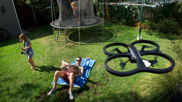 A drone helicopter which can record video and photos hovers above a suburban back yard.