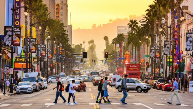 Pedestrians cross traffic on Hollywood Boulevard at dusk, Los Angeles.