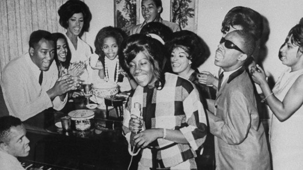 Berry Gordy playing piano in 1964 with Smokey Robinson (at top of photo) and Stevie Wonder (second from right).