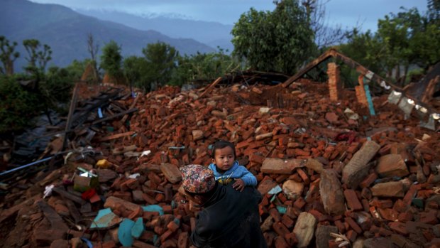 A local villager walks carrying a child amid debris at a devastated area in Gorkha, one of the worst hit regions. 