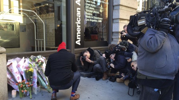 A fan lays a bouquet of flowers outside David Bowie's apartment building in Manhattan as the media scrum looks on. 