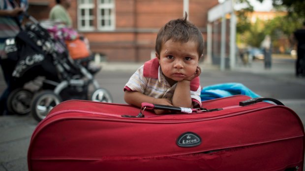 A migrant boy waits at his parents' suitcase as they leave the Berlin State Office for Health and Social Affairs with other newly arrived refugees on Monday.