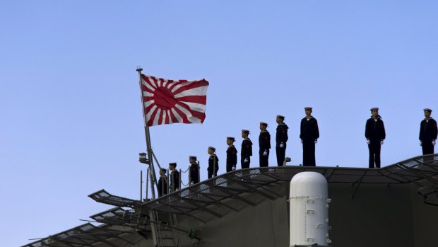 Sailors stand on the deck of the Izumo warship as it departs a shipyard in Yokohama.