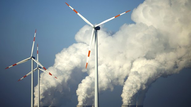 Steam billows from the cooling towers of brown coal power station behind wind turbines near Cottbus, eastern Germany